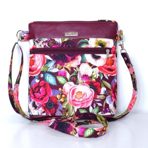 Pu&ograve; includere: Una borsa a tracolla color bordeaux con stampa floreale. La borsa ha una chiusura a zip e una lunga tracolla regolabile.