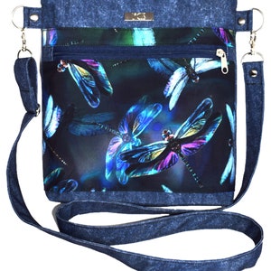 Pu&ograve; includere: Una borsa a tracolla in denim con stampa libellula blu scuro e viola. La borsa ha una tasca con cerniera e una lunga tracolla regolabile.
