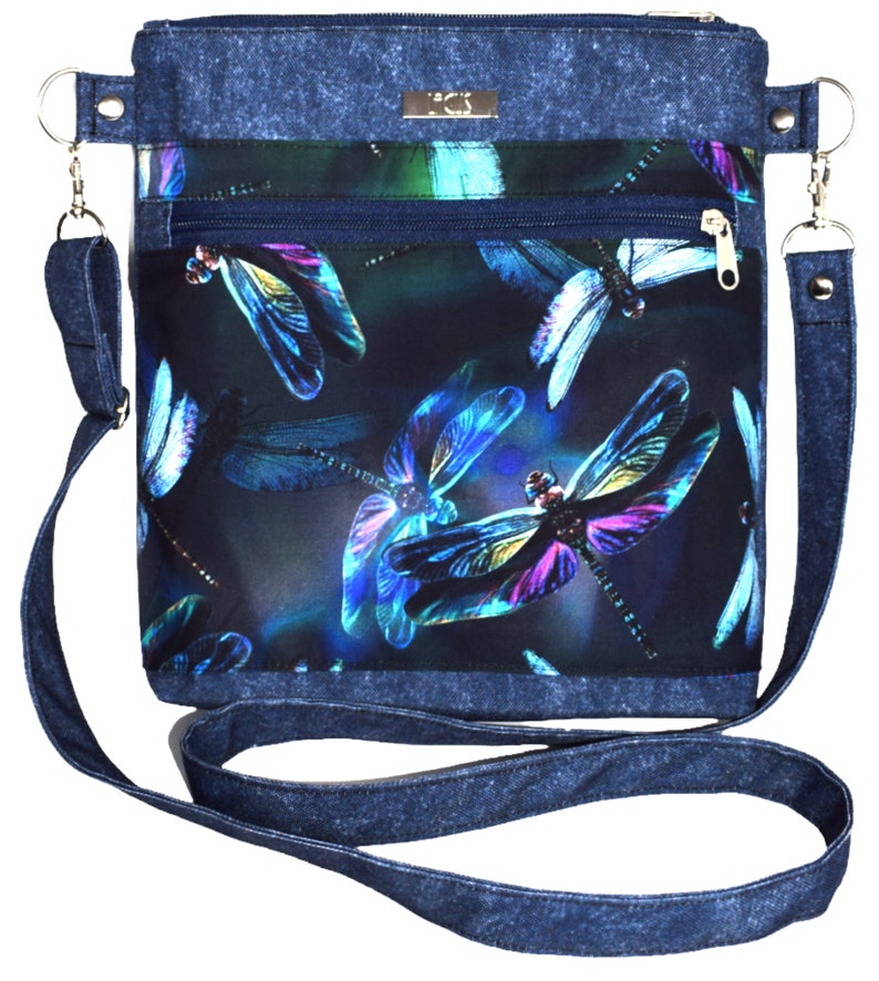 Pu&ograve; includere: Una borsa a tracolla in denim con stampa libellula blu scuro e viola. La borsa ha una tasca con cerniera e una lunga tracolla regolabile.