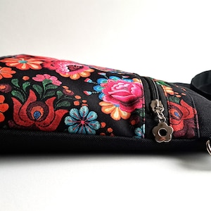 Pu&ograve; includere: Una borsa a tracolla nera con stampa floreale e una tasca con cerniera. La borsa ha una tracolla nera e una chiusura argentata.