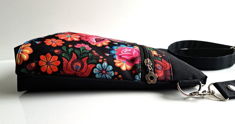 Pu&ograve; includere: Una borsa a tracolla nera con stampa floreale e una tasca con cerniera. La borsa ha una tracolla nera e una chiusura argentata.