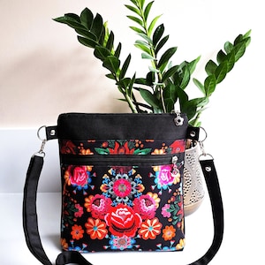 Pu&ograve; includere: Una borsa a tracolla nera con una stampa floreale con fiori rossi, rosa, arancioni, gialli, blu e verdi. La borsa ha una chiusura a zip e una tracolla regolabile.