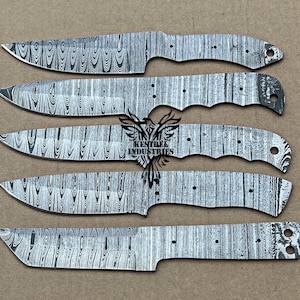 May include: Five unfinished Damascus steel knife blades with a wood grain pattern. The blades vary in shape, with some having a curved edge and others a straight edge. The blades are silver and black, and are arranged on a tan surface.
