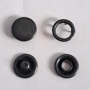 May include: Four dark gray metal snap fasteners. The set includes a solid circular cap, a ring with a prong, and two snap components with a central stud and a socket. These fasteners are commonly used in clothing and accessories.