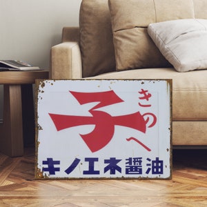 Könnte beinhalten: Ein vintage, rostiges Metallschild mit einem roten und weißen Logo einer stilisierten Nummer drei. Das Schild trägt die Aufschrift "キノのキハエ末 醤油" in japanischen Schriftzeichen.
