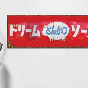 Könnte beinhalten: Ein rotes, rostiges Metallschild mit weißer Aufschrift, die "Dream Pork Sauce" lautet. In der Mitte des Schildes ist ein Comic-Schwein abgebildet.
