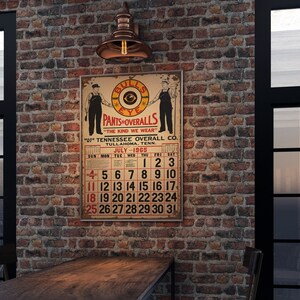May include: A vintage poster advertising "Bulls Eye Pants & Overalls" with a calendar for July 1965. The poster is hanging on a brick wall with a copper light fixture above it.