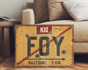 May include: A vintage-style yellow road sign with red and black accents. The sign reads "N30 FOY BASTOGNE 5 KM" and has a red diagonal line across it with an arrow pointing to the right.