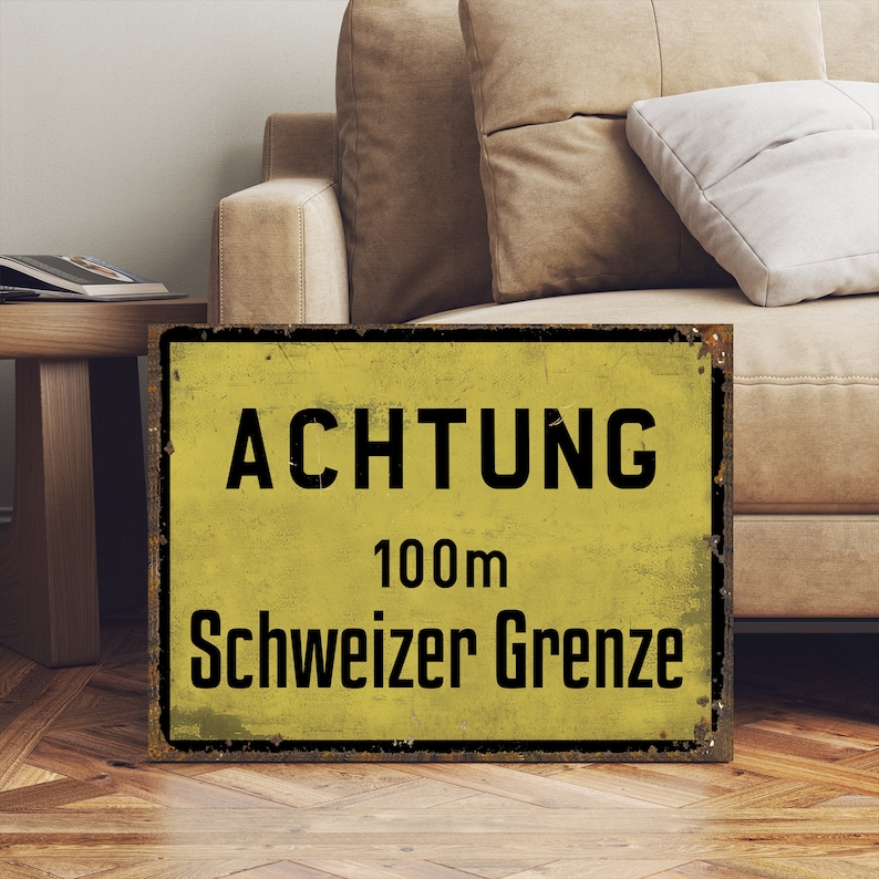 May include: A yellow and black metal sign with the text "ACHTUNG 100m Schweizer Grenze".