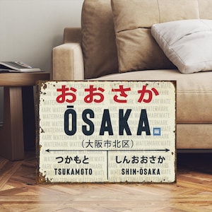May include: A rectangular, distressed metal sign featuring the word "OSAKA" in large, dark blue letters. Above, the Japanese word for Osaka is in red. Below, Japanese text and arrows indicate locations. The sign has a vintage, weathered appearance.