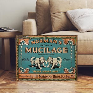 Könnte beinhalten: Vintage Schild für Norman's Indian Mucilage. Das Schild zeigt einen türkisfarbenen Hintergrund mit den Worten "Norman's Indian Mucilage" und zwei Bulldoggen-Illustrationen. Das Schild enthält auch den Text "Never Leaves Grip" und "Manufactured by H.D. Nariman Bros. Bombay, No. 2."