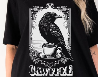 May include: Black t-shirt with a white graphic of a raven perched on a coffee cup. The graphic is framed with an ornate design and the text "CAWFFEE" is below the image.