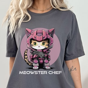 May include: A gray t-shirt with a cartoon cat wearing pink and purple armor and holding a gun. The text "MEOWSTER CHIEF" is printed below the cat.