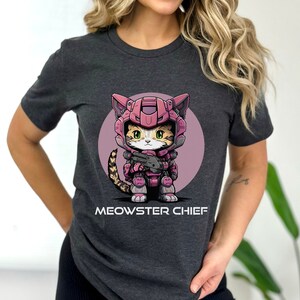 May include: A dark gray t-shirt with a cartoon illustration of a cat wearing pink and gray armor and holding a gun. The text "MEOWSTER CHIEF" is printed below the image.