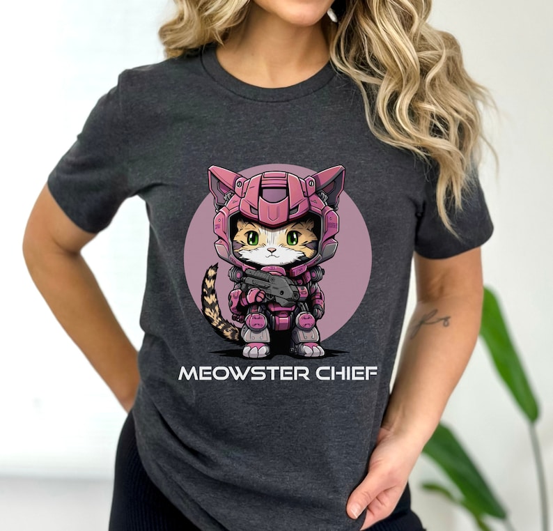 May include: A dark gray t-shirt with a cartoon illustration of a cat wearing pink and gray armor and holding a gun. The text "MEOWSTER CHIEF" is printed below the image.