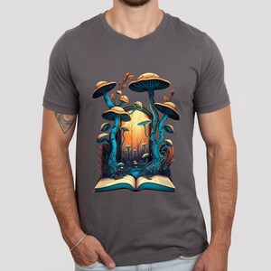 May include: Dark gray t-shirt featuring a vibrant illustration of mushrooms emerging from an open book. The artwork showcases blue and orange tones, with detailed mushroom caps and a forest scene. The design is centered on the shirt.