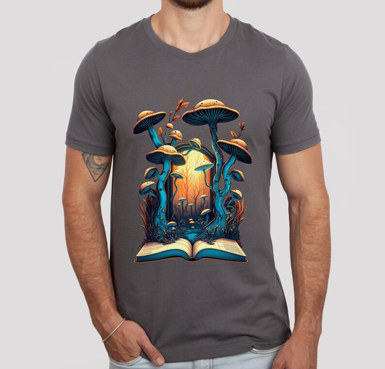 May include: Dark gray t-shirt featuring a vibrant illustration of mushrooms emerging from an open book. The artwork showcases blue and orange tones, with detailed mushroom caps and a forest scene. The design is centered on the shirt.