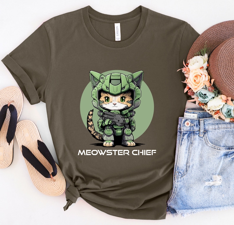 Puede incluir: Camiseta verde oliva con un gato de dibujos animados con casco y armadura militar verde, sosteniendo un arma. El texto "MEOWSTER CHIEF" est&aacute; impreso debajo de la ilustraci&oacute;n del gato. La camiseta se muestra con un sombrero de paja y pantalones cortos de mezclilla.