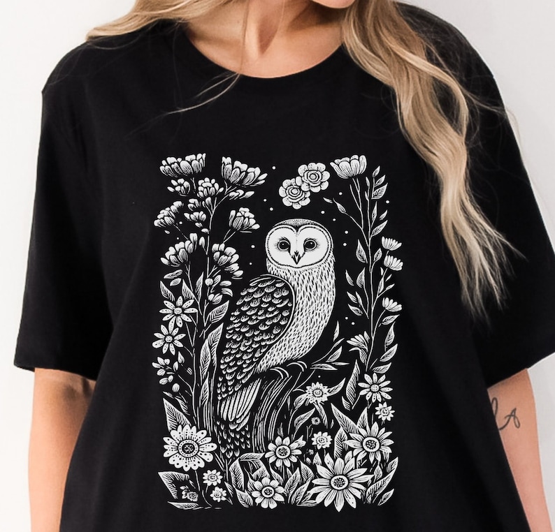May include: Black t-shirt with a white graphic print of an owl surrounded by flowers.