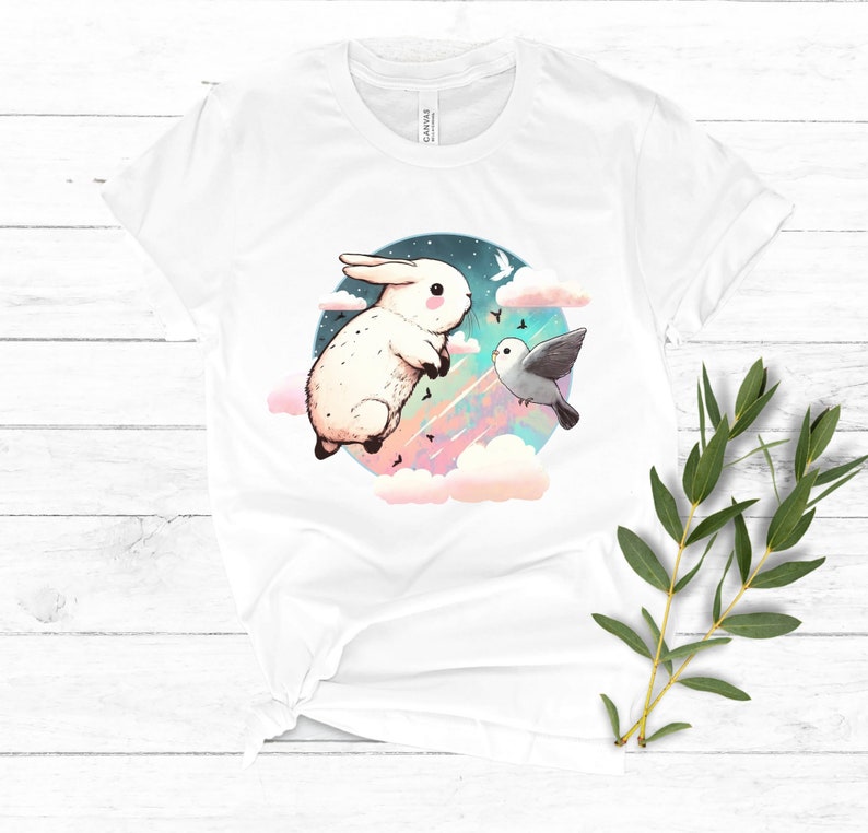 May include: White t-shirt with a graphic of a white rabbit and a gray bird flying in a colorful sky with clouds.