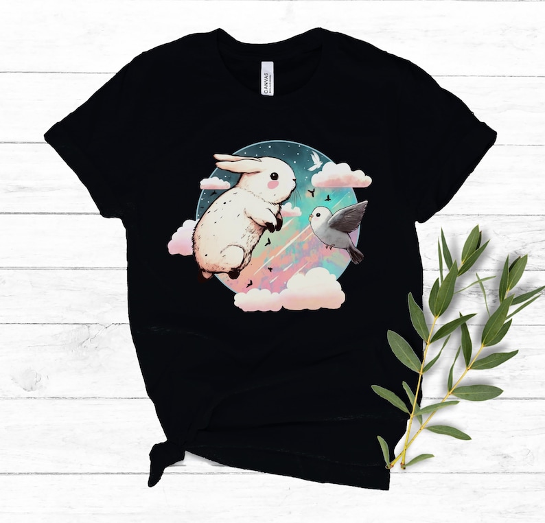 May include: Black t-shirt with a white rabbit and a bird flying in a circle of clouds against a dark blue background with stars and a rainbow.