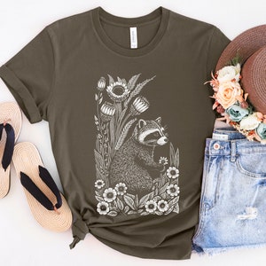 May include: A dark green t-shirt with a white graphic of a raccoon surrounded by flowers. The raccoon is looking to the right and holding a flower in its paw.