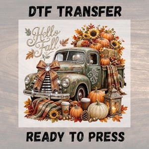 Puede incluir: Una transferencia DTF con un camión verde antiguo con un gran lazo naranja en la parrilla, cargado de calabazas, girasoles y hojas de otoño. El texto dice DTF TRANSFER, Hello Fall y READY TO PRESS, junto a una linterna y una manta a cuadros.