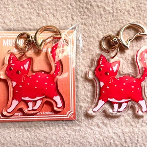 Può includere: Due portachiavi con ciondolo a forma di gatto macchiato rosso e bianco. I ciondoli sono in acrilico trasparente e hanno un anello portachiavi in metallo dorato. I ciondoli sono confezionati in sacchetti di plastica trasparenti.