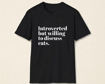 May include: A black short-sleeved t-shirt featuring white text printed on the front that reads: Introverted but willing to discuss cats. The garment has a classic crew neckline and a standard fit, presented against a neutral, light-coloured background.