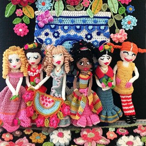 May include: Seven crocheted dolls in various colors and styles stand in front of a crocheted flower arrangement in a blue and white vase. The dolls are wearing dresses and skirts with colorful details. The flowers are in shades of pink, red, orange, yellow, and blue.