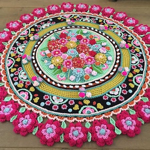 Peut inclure: Un tapis rond en crochet de style mandala avec un motif floral dans des tons de rose, vert, jaune et orange. Le tapis a un centre noir avec une bordure multicolore.