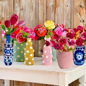 Peut inclure: Un assortiment de fleurs crochetées colorées dans différents vases. Les fleurs comprennent des tulipes rouges, des roses roses et des fleurs jaunes. Les vases sont décorés de motifs crochetés bleus, verts, jaunes et roses, certains à pois blancs.