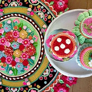 Peut inclure: Un tapis en crochet en forme de mandala avec un motif floral dans des tons de rose, rouge, vert et jaune. Trois g&acirc;teaux en crochet avec un gla&ccedil;age rose, vert et blanc sont pr&eacute;sent&eacute;s sur un plateau blanc.