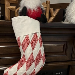 May include: A festive Christmas stocking with a red and white diamond pattern. The stocking features a white cuff with small white polka dots. The word "Family" is visible in wooden letters in the background.