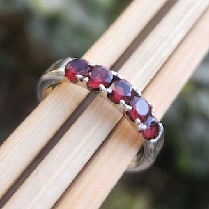 May include: A silver band ring with a row of six red gemstones. The ring is on a wooden surface.