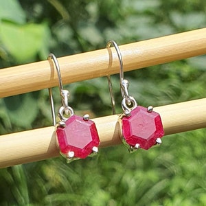 Op de afbeelding: Een paar zilveren oorbellen met rode edelsteen druppels. De edelstenen zijn gefacetteerd en hebben een zeshoekige vorm.
