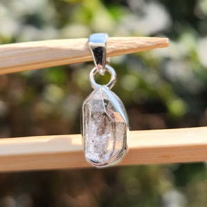 May include: A silver pendant featuring a clear, faceted crystal with a silver bail.