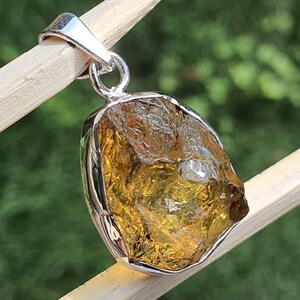 May include: A silver pendant featuring a large, raw, golden citrine gemstone. The gemstone is set in a silver bezel and has a rough, natural texture.