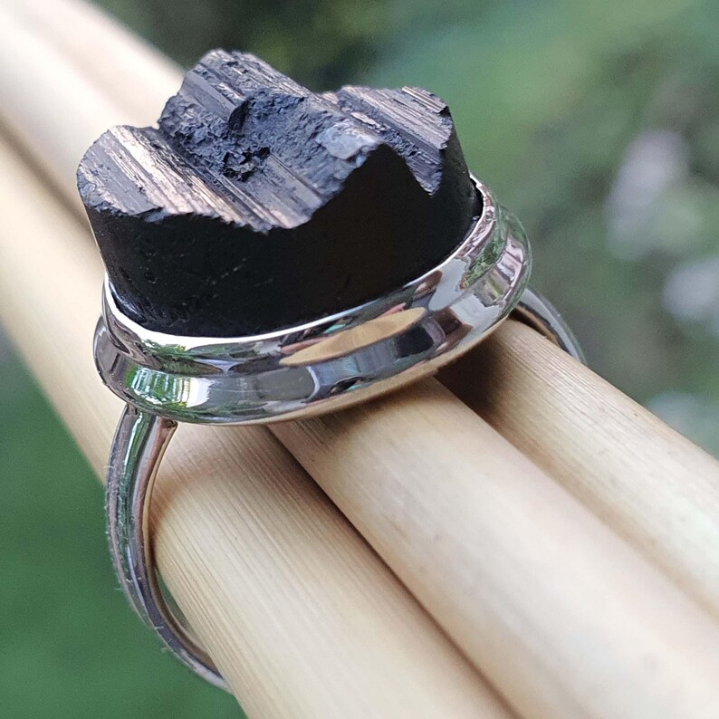 Op de afbeelding: Een zilveren ring met een zwarte, ruwe steen gezet in een bezel setting. De ring ligt op een houten oppervlak.