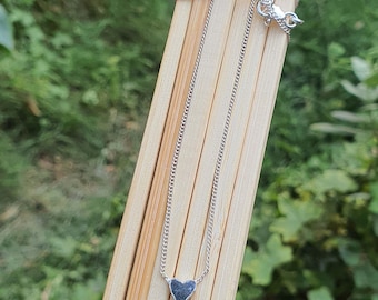 May include: A silver chain necklace with a small, dark gray heart pendant.