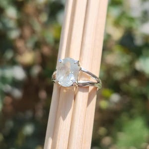 May include: A silver ring featuring a large, oval-shaped, translucent light blue gemstone held in a four-prong setting. The band of the ring has a textured, organic, branch-like appearance with a polished metallic finish.