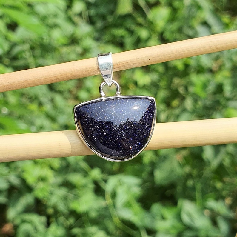 May include: A silver pendant with a dark blue, semi-precious gemstone. The gemstone is a half-moon shape and has a sparkly, glittery texture.