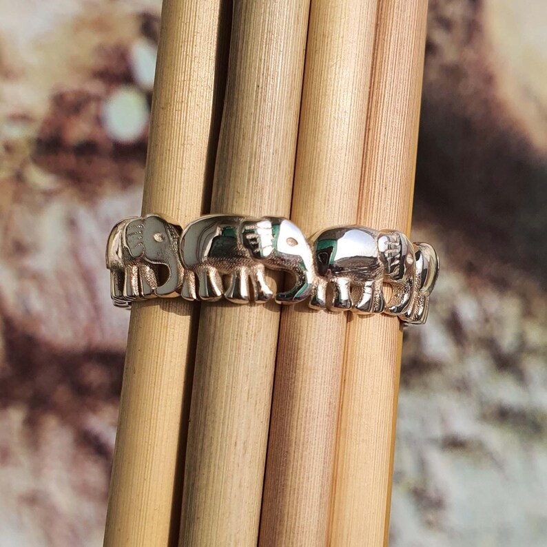 May include: A silver ring featuring a repeating elephant design. The ring is made of shiny metal and has a detailed, three-dimensional appearance. The elephants are arranged in a row, creating a continuous pattern around the band.