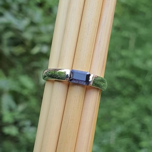 May include: A silver ring with a dark purple rectangular gemstone.