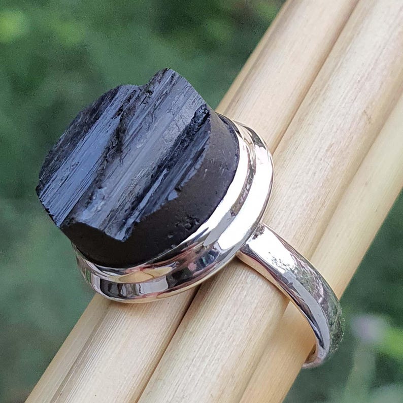 Op de afbeelding: Een zilveren ring met een zwarte, ruwe edelsteen. De edelsteen is gezet in een zilveren bezel en de ringband is glad.