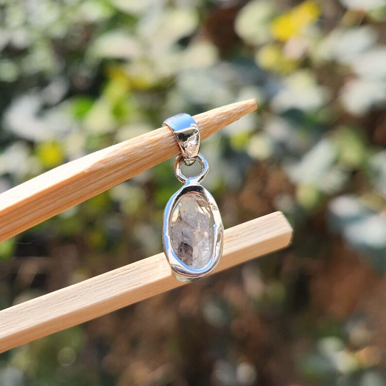 May include: A silver pendant featuring a clear, faceted, oval-shaped crystal.