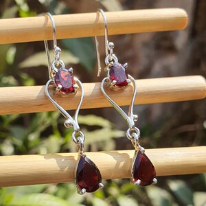 Puede incluir: Un par de pendientes colgantes de plata con piedras preciosas rojas de forma ovalada y de l&aacute;grima. Los pendientes est&aacute;n suspendidos de un gancho y presentan un dise&ntilde;o en forma de coraz&oacute;n. Las piedras son de color rojo intenso.