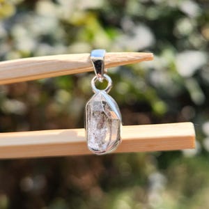 May include: A silver pendant featuring a clear, faceted crystal with a silver bail.