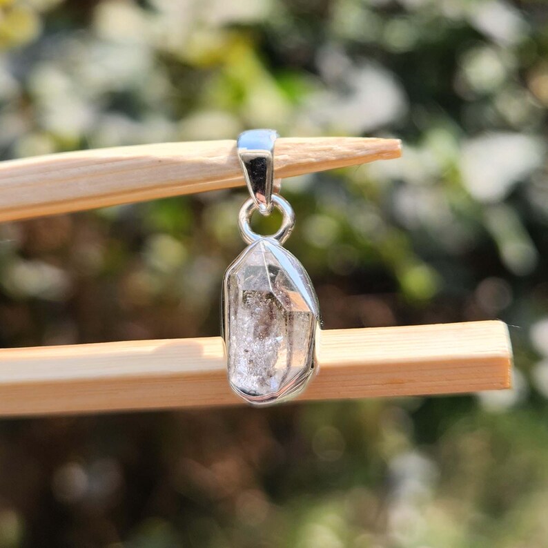 May include: A silver pendant featuring a clear, faceted crystal with a silver bail.