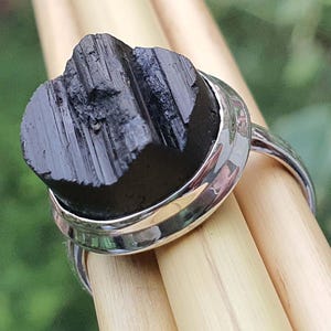 Op de afbeelding: Een zilveren ring met een zwarte, ruwe, natuurlijke steen in een bezel-setting. De steen heeft een gestreepte textuur.